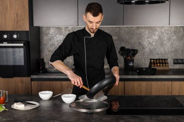 Mutfakta siyah üniformalı bir aşçı yemek pişirmek için malzemelerle hazırlandı. Şef kahvaltıda domuz pastırmalı omlet yapıyor..