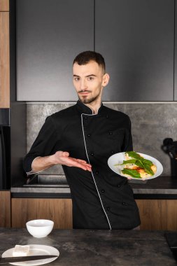 Mutfakta tabağıyla birlikte siyah üniformalı tatmin olmuş ve memnun bir aşçı. Şefin sağlıklı bir kahvaltısı var..
