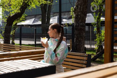 Genç, sıska esmer kız fast food sosisli sandviç ya da açık havada hamburger yiyor..