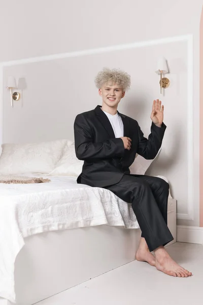Młody Kręcony Blondyn Wyglądający Jak Lalka Siedzący Łóżku Udaje Lalkę — Zdjęcie stockowe