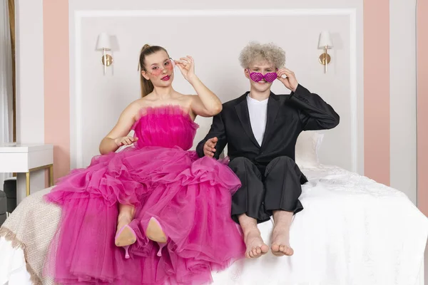 グラマーの少女と人形のように見える男がベッドの上に座っている 人形カップル服を着て長いピンクのドレスと黒のスーツ — ストック写真