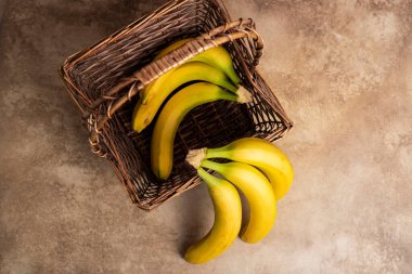 Hasır bir sepetin içinde, ahşap bir arka planda muzlar. Üst görünüm, düz görünüm, kopyalama alanı.