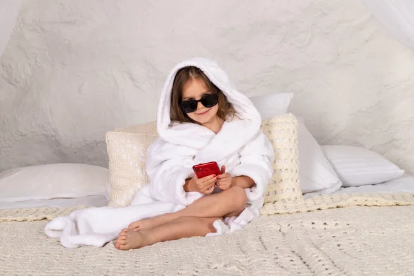 Schattig Gelukkig Klein Meisje Witte Badjas Zonnebril Ligt Een Bed — Stockfoto