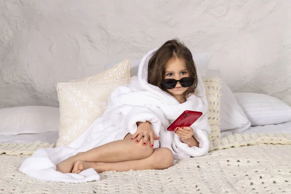 가운을 선글라스를 소녀가 침대에 그녀의 전화기를 있습니다 — 스톡 사진
