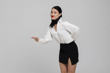 Çekici genç bir hostesin portresi. Çekici, güler yüzlü, seksi üniformalı, el kol hareketi yapan, içeri girmeyi teklif eden bir hostes. Beyaz arkaplanda izole.