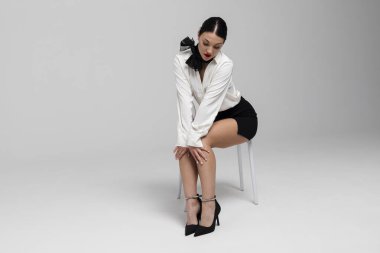 Çekici genç bir hostesin portresi. Çekici, güler yüzlü, seksi üniformalı, sandalyede poz veren bir hostes. Beyaz arkaplanda izole.