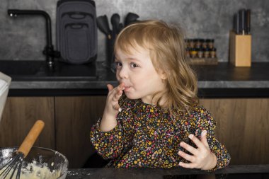 Küçük kardeşler modern bir mutfakta birlikte yemek pişiriyor, birbirlerine yardım ediyor ve eğleniyorlar, annem yokken çiğ hamur yiyorlar..
