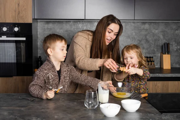 stock image Mother cooking together with her children on a modern kitchen, helping each other and having fun. Nanny teaches kids to cook.