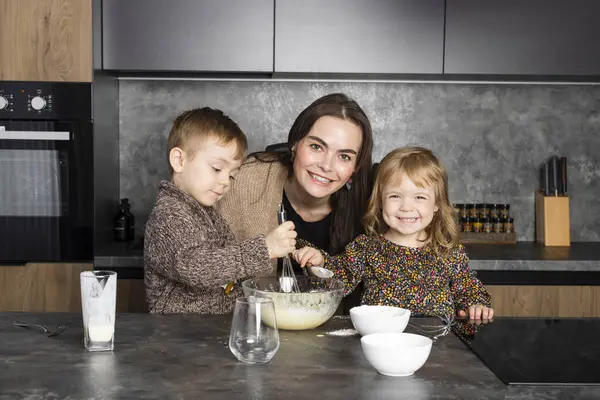 Anne çocuklarıyla birlikte modern bir mutfakta yemek pişiriyor, birbirine yardım ediyor ve eğleniyor. Dadı çocuklara yemek yapmayı öğretiyor..