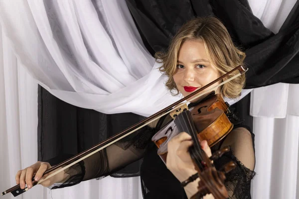 バイオリンを弾いている若いエレガントなブロンドの女の子 黒と白のカーテンに対する女性ヴァイオリニストの肖像 — ストック写真