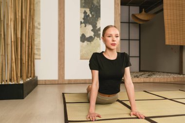 Sıska sarışın kız yoga yapıyor, egzersiz yapıyor, ısınıyor spor kıyafetleri giyiyor, pantolon ve bluz giyiyor, Japon tarzı bir stüdyoda..