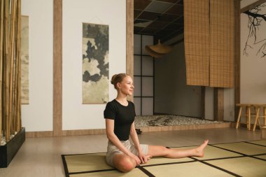 Sıska sarışın kız yoga yapıyor, egzersiz yapıyor, ısınıyor spor kıyafetleri giyiyor, pantolon ve bluz giyiyor, Japon tarzı bir stüdyoda..