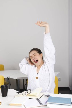 Genç kız öğrenci ödevini yapmaktan, sınıfta esnemekten yoruldu. Masadaki dağınıklık, kitaplar, defterler, malzemeler. Şirin kız, saçları topuz gibi bağlanmış..