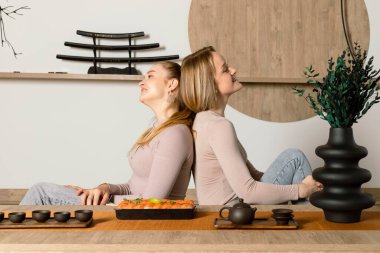 Çekici genç ikiz kardeşler suşi yer ve Japon tarzı bir odada sırt sırta oturarak çay içerler..