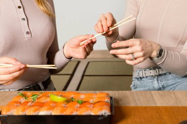 Büyük bir suşi seti ve Japon çay fincanları. Arka planda çubukları olan iki kız..