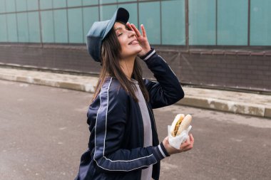 Spor takım elbiseli esmer kız dışarıda fast food burger yiyor..