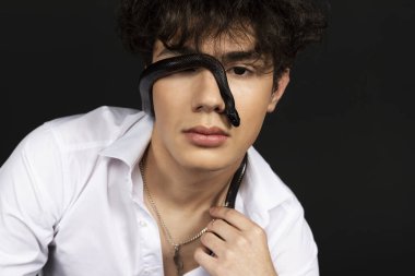 Yüzünde siyah bir yılan olan beyaz gömlekli genç yakışıklı bir adam. Siyah arkaplanda izole.