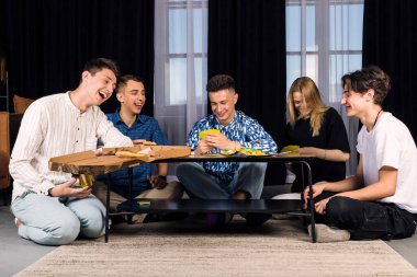 Beş arkadaş birlikte vakit geçiriyorlar, eğleniyorlar, masa oyunları oynuyorlar ve fast food ve abur cubur yiyorlar. Oturma odasında küçük bir arkadaş grubu..