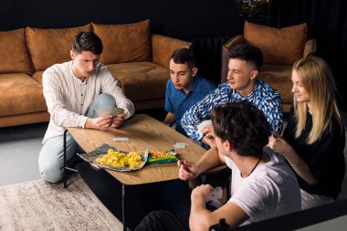 Beş arkadaş birlikte vakit geçiriyorlar, eğleniyorlar, masa oyunları oynuyorlar ve fast food ve abur cubur yiyorlar. Oturma odasında küçük bir arkadaş grubu..