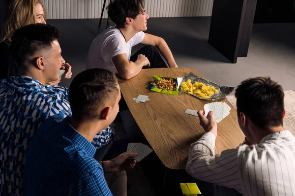 Five friends spending time together, having fun, playing table games and eating fast food and snacks. Small group of friend in a living room.