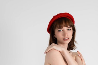Genç ve güzel bir kız sadece kırmızı sıkı ve bereli, çıplak göğsünü kapatıyor. Üstsüz poz veren seksi zayıf kız. Beyaz arka planda izole edilmiş. Portre, kafasından..