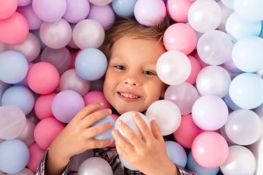 Plastik toplarla dolu bir havuzda küçük bir çocuk. Çocuklar için pastel renkli plastik topları dikizleyen bir çocuk. en üstteki görünüm.