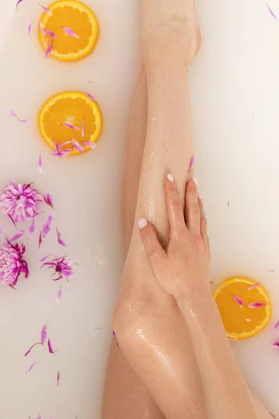 柔嫩的女孩的腿在一个充满橘子片和花瓣的浴池中 美容美发的概念 顶部视图 — 图库照片