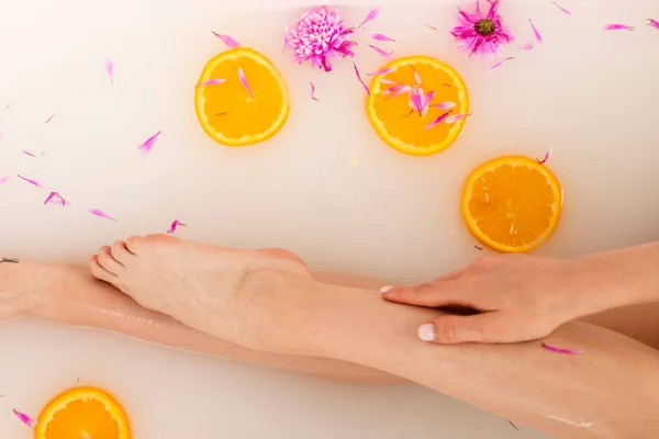 柔嫩的女孩的腿在一个充满橘子片和花瓣的浴池中 美容美发的概念 顶部视图 — 图库照片