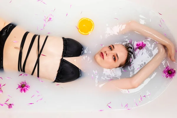 温柔的女孩躺在一半的水里沐浴 里面塞满了橘子片和花瓣 美容美发的概念 顶部视图 — 图库照片