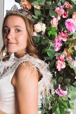 Zarif beyaz elbiseler içinde güzel bir gelin bitkilerin önünde taç ve çiçekli bir kemer. Bahçedeki gelin..