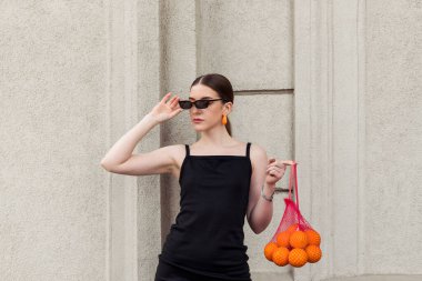 Giyim kuşamında ve makyajında belirgin turuncu unsurları olan güzel, modaya uygun genç bir kız sokakta poz veriyor..