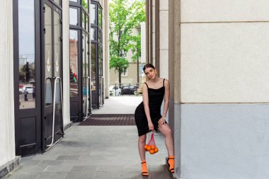 Giyim kuşamında ve makyajında belirgin turuncu unsurları olan güzel, modaya uygun genç bir kız sokakta poz veriyor..