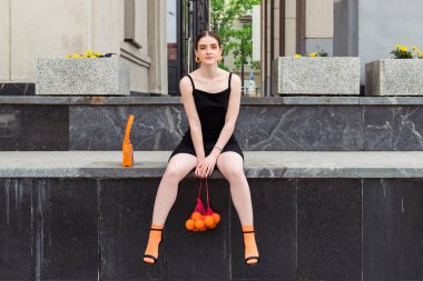 Giyim kuşamında ve makyajında belirgin turuncu unsurları olan güzel, modaya uygun genç bir kız sokakta poz veriyor..