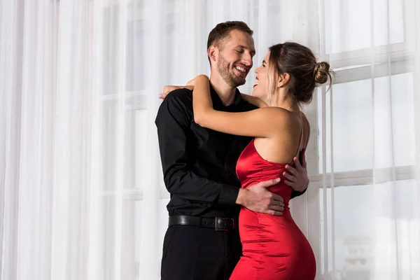赤のドレスで黒と美しい女性のハンサムなよく服を着た若い男が密接にお互いを見ている ロマンチックなカップル交換愛の視線で互い — ストック写真