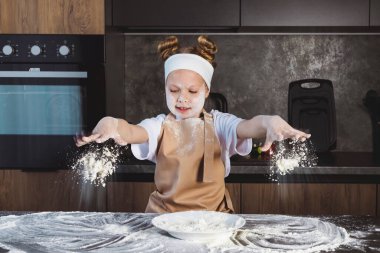 Çocuklar için aşçılık ya da aşçılık okulu. Una bulanmış elleri ve yüzü olan küçük bir kız masaya un döker, hareketli bir atış yapar..