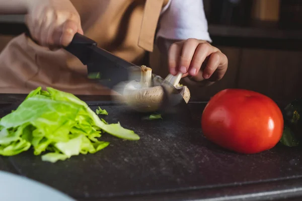 stock image Little girl cooks on the kitchen, preparing ingredients, cutting vegetables, in motion shot.