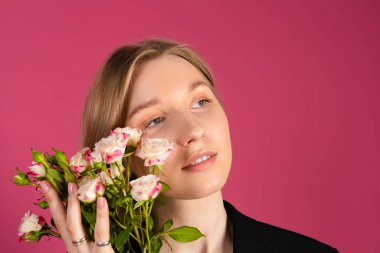 Siyah ceketli güzel, narin sarışın kız elinde çiçekler tutuyor. Pembe arkaplanda izole.