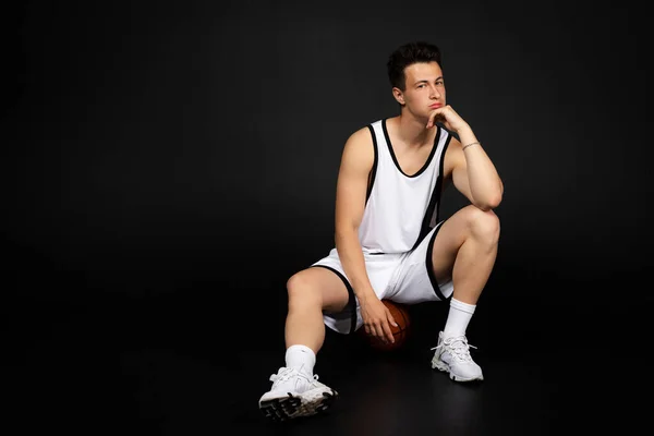 Stilig Ung Basketspelare Vita Sportkläder Sitter Boll Isolerad Svart Bakgrund — Stockfoto