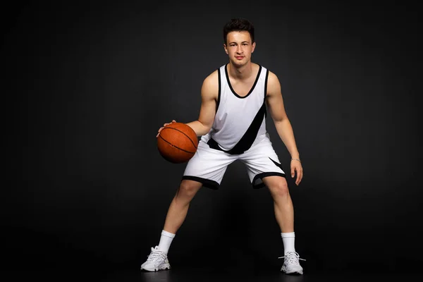 ミンスク ベラルーシ 2023年5月22日 白のスポーツウェアを着たハンサムな若いバスケットボール選手がボールと一緒に 黒の背景に隔離された — ストック写真
