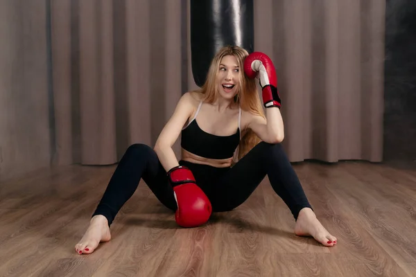 タイトな黒のスポーツウェアとボクシングの手袋を身に着けている魅力的なスポーティーな女の子 パンチバッグでトレーニング 煙とジムでポーズ ストック画像
