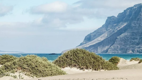 Plaj ve Dağlar - Caleta de Famara 'nın güzel kıyıları, Lanzarote Kanarya Adaları. Caleta de Famara 'daki plaj sörfçüler arasında çok popüler..