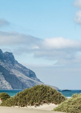 Plaj ve Dağlar - Caleta de Famara 'nın güzel kıyıları, Lanzarote Kanarya Adaları. Caleta de Famara 'daki plaj sörfçüler arasında çok popüler..