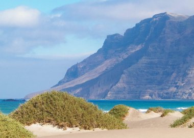 Plaj ve Dağlar - Caleta de Famara 'nın güzel kıyıları, Lanzarote Kanarya Adaları. Caleta de Famara 'daki plaj sörfçüler arasında çok popüler..