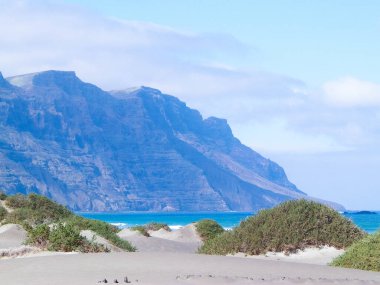 Plaj ve Dağlar - Caleta de Famara 'nın güzel kıyıları, Lanzarote Kanarya Adaları. Caleta de Famara 'daki plaj sörfçüler arasında çok popüler..