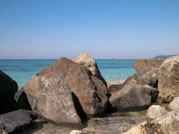 Vada sahilindeki taşlar, şeffaf, turkuaz su ve beyaz kum. Seyahat ve doğa kavramı.