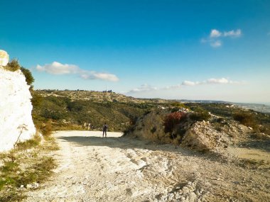 Yaz mevsiminde bir turist dağ yolunda yürüyor. Kıbrıs adasındaki Troodos Dağları. Paphos bölgesine yakın. Boşluğu mavi gökyüzünde kopyala.