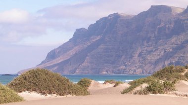 Plaj ve Dağlar - Caleta de Famara 'nın güzel kıyıları, Lanzarote Kanarya Adaları. Caleta de Famara 'daki plaj sörfçüler arasında çok popüler..
