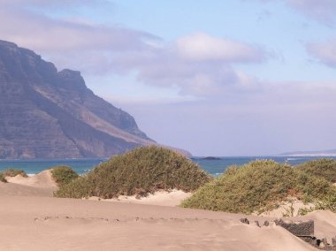Plaj ve Dağlar - Caleta de Famara 'nın güzel kıyıları, Lanzarote Kanarya Adaları. Caleta de Famara 'daki plaj sörfçüler arasında çok popüler..