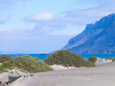 Plaj ve Dağlar - Caleta de Famara 'nın güzel kıyıları, Lanzarote Kanarya Adaları. Caleta de Famara 'daki plaj sörfçüler arasında çok popüler..