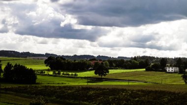 Rainy day over green hills and meadows of Kashubian Region, Poland. Copy space on cloudy sky.